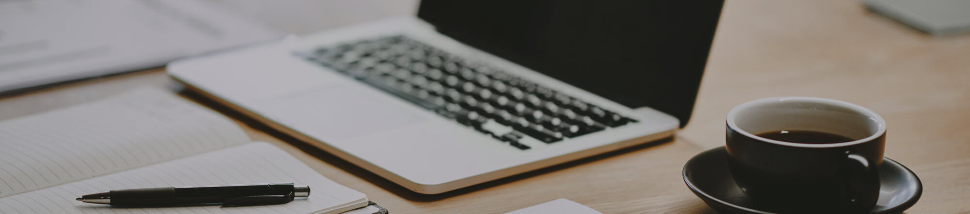 laptop, coffee cup, notepad and pen on a wooden table